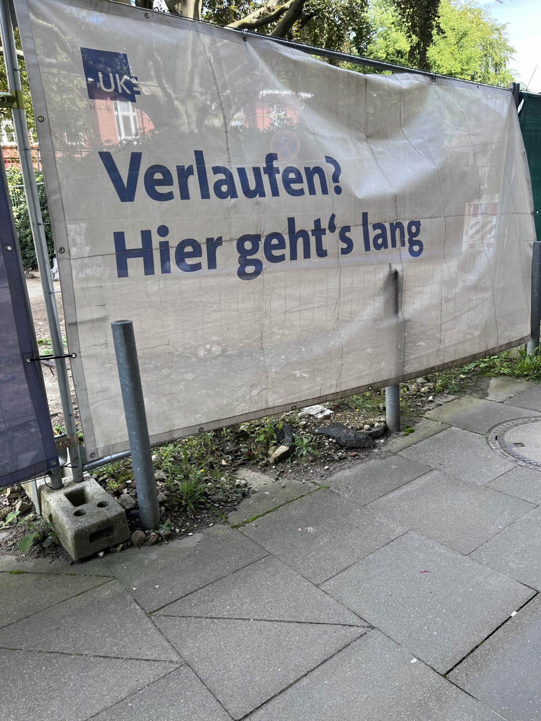 Baustellenabdeckung am Zaun mit Beschriftung: "Verlaufen? Hier geht´s lang" und "UKE"